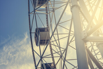 Gray or white metal ferris wheel with closed passenger cabins close-up in the amusement park