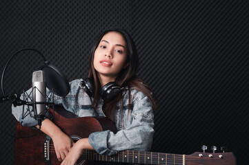 Asian female singer with a passion for music and microphone. While playing her guitar in a professional studio. Music concept, sound recording concept.