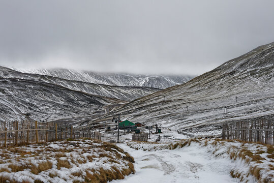 The view from a ski run above the Cairnwell Cafe at the Ski Resort of Glenshee with light snow covering the ground, and dark low clouds above.