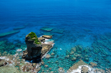 Impressive transparent blue sea seen from a cliff where you can see the famous Tategami Iwa stone sorrounded by coral reefs. Yonaguni Island.