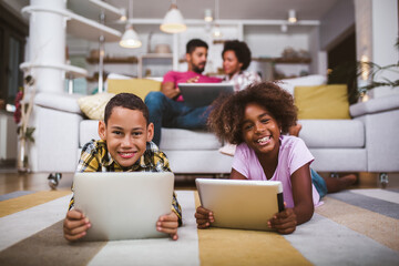African american boy and girl lying on floor and using digital tablet. Family at home.