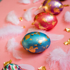 Obraz na płótnie Canvas Painted eggs with golden foil and white feathers on the pink background.