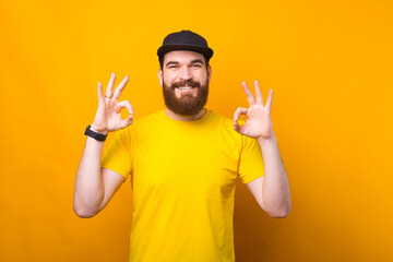 Naklejka premium Photo of joyful young man in yellow shirt showing OK gesture and smiling at camera.