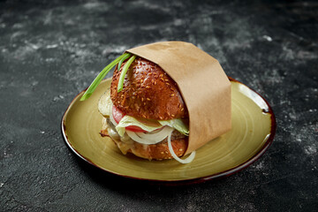 Juicy and appetizing burger with beef, lettuce, mozzarella and tomatoes on a vintage plate on a wooden background. Close up, selective focus. Noise grain added on post