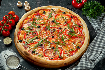 Obraz na płótnie Canvas Oven-baked Italian pizza with sauce, cheese, mushrooms, bell peppers and olives in a composition with ingredients on a dark background. Top view. Vegetarian pizza