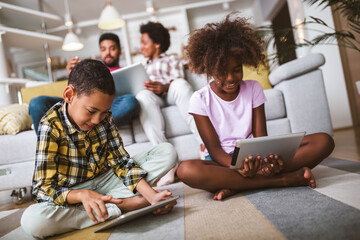 African american boy and girl lying on floor and using digital tablet. Family at home.