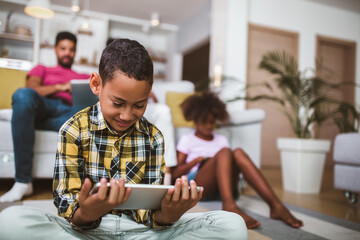 African american boy and girl lying on floor and using digital tablet. Family at home.