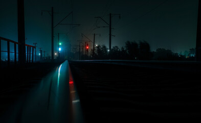 Empty railroad at night. Red and green traffic lights. A strong wind shakes the trees.