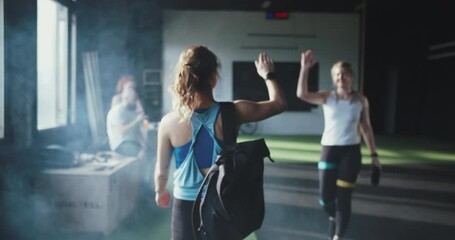 Athletic lifestyle community. Rear view young fit blonde woman enters large gym to work out, high-fives happy friends.