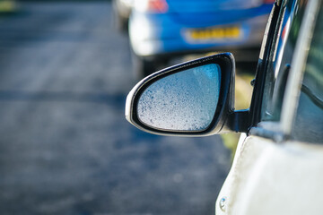 Dew drops on rear view mirror of a white car with sunshine in morning.