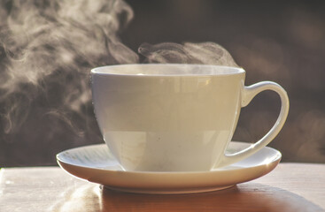 Hot tea cup on a frosty winter day put on wooden table with background of front garden in morning.