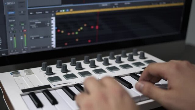 Male hands recording music, playing electronic keyboard, midi keys on the table. Closeup of male hands composing music in sequencer using midi keyboard with keys and pads