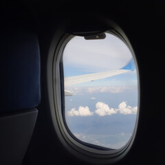 Outlook through plane window while traveling with window surround framing blue sky and clouds with focus on wing outside.