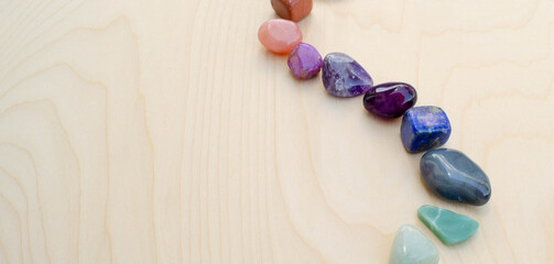 Rainbow colored polished rocks curving across a wood background
