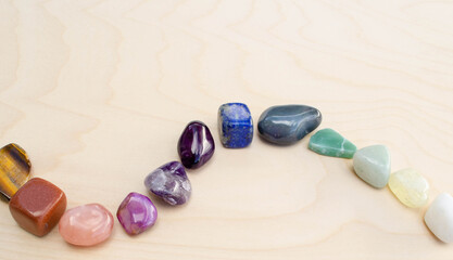 Rainbow colored polished rocks curving across a wood background
