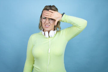 Young caucasian woman wearing headphones on neck over blue background Touching forehead for illness and fever, flu and cold, virus sick