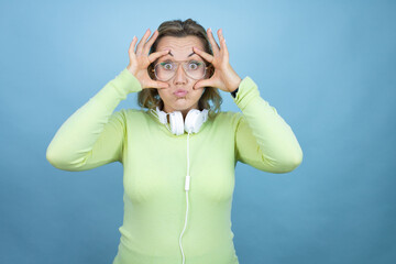 Young caucasian woman wearing headphones on neck over blue background Trying to open eyes with fingers, sleepy and tired for morning fatigue