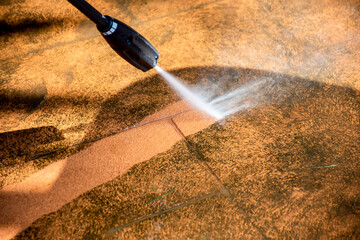 Cleaning backyard paving tiles with pressure washer.