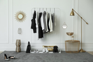 Rack with stylish clothes near white wall in dressing room