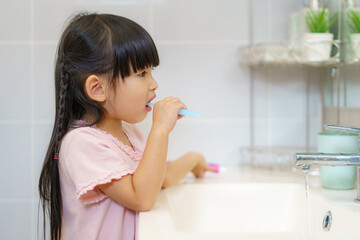 Asian cute child girl or kid brushing her teeth by toothbrush in the bathroom. Dental hygiene Healthcare concept.