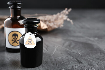 Glass bottles of poison with warning signs on grey stone table. Space for text