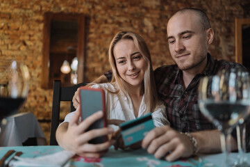 Close up of happy young Caucasian couple shopping online on smartphone using credit card - Smiling millennial man and woman make payment purchase on web by cell phone .
