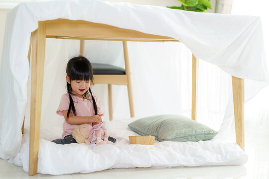 Asian Cute Little Girl Play Her Doll While Sitting In A Blanket Fort In Living Room At Home For Perfect Hideout Away From Their Other Family Members And For Them To Play Imaginatively.