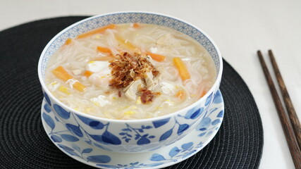 Vietnamese noodles with fried red onions on top, served in a white and blue bowl and chopstick on the side