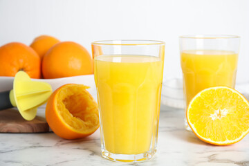 Fototapeta na wymiar Fresh ripe oranges, juice and reamer on white marble table