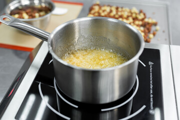 Steel pan with boiling and bubbling sugar mass for making caramel.