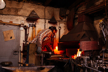 The blacksmith manually forging the molten metal on the anvil in smithy.