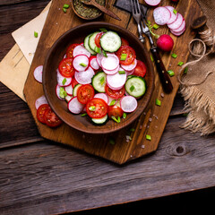 tasty spring salad with round sliced tomatoes, cucumber, radish in wooden bowl on rustic table