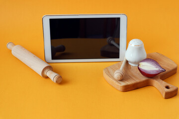 Tablet, wooden board, rolling pin on a yellow background, side view-the concept of conducting cooking courses via the Internet
