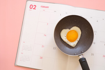 Heart shape fried egg in the pan on the calendar isolated on pink background. top view. Valentine's day concept. Copy space for text