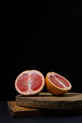 Grapefruit on a black background. Grapefruit cut in half on a wooden board. Citrus fruit. Exotic fruit