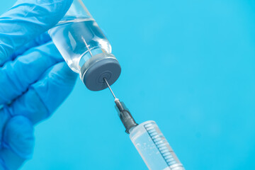 Hands in blue gloves dials medicine using a syringe with a needle from a medical bottle on a blue background with copy space. Concept of medicine, vaccination