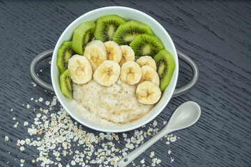 Oatmeal porridge with bananas, kiwi in in a bowl on a dark background, top view. Healthy breakfast