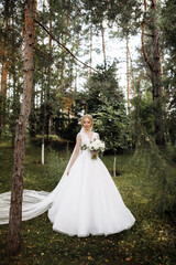 Fototapeta premium bride in a dress standing in a green garden and holding a wedding bouquet of flowers and greenery
