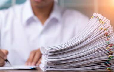 Male office workers holding and writing documents on office desk with light fair, Stack of business overload paper and paperless concept.