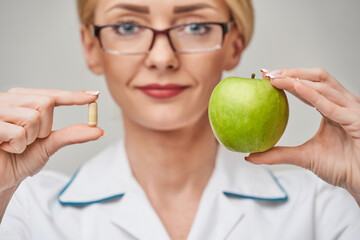 nutritionist doctor healthy lifestyle concept - holding organic fresh green apple and vitamin...