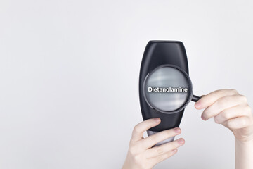 Chemical components on the shampoo label: Dietanolamine. Female hands hold a magnifying glass on the jar, which indicates the harmful ingredient. White background, place for your text