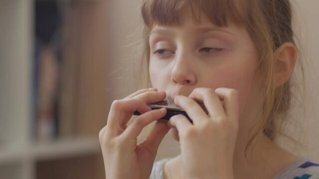 Cheerful girl playing the harmonica home interior closeup
