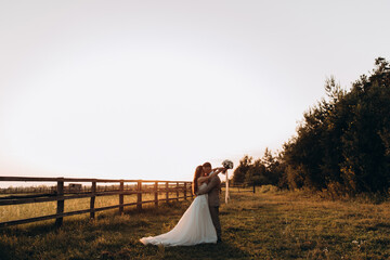 Walk the newlyweds at sunset. The bride and groom in the rays. Evening landscape.