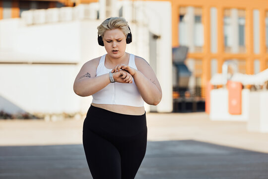 Curvy woman in sportswear checking an app on a smartwatch while running on roof 