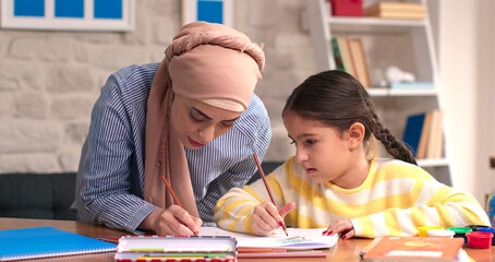Little girl doing homework with her mother wearing a headscarf. Study. Fun learning concept.