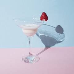 Cocktail glass with a milk and strawberry on pastel pink and blue background. Stay at home concept party.