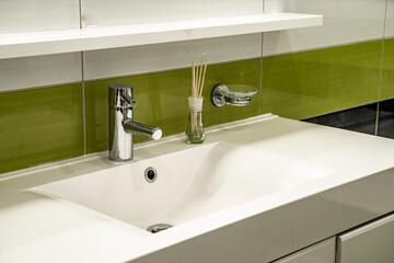 Close-up of white sink in modern bathroom. Green, black and white tile. Aroma sticks.