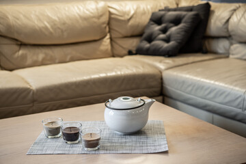 Close-up of teapot and candles on coffee table near cozy couch. Modern interior of living room.