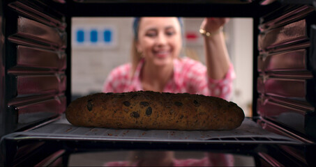 Pretty woman with blonde hair takes out delicious, rich grain and olive bread from the oven....