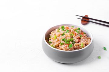 Fried rice with vegetables and egg in the gray ceramic bowl on the white table. Chinese food. Copy space
